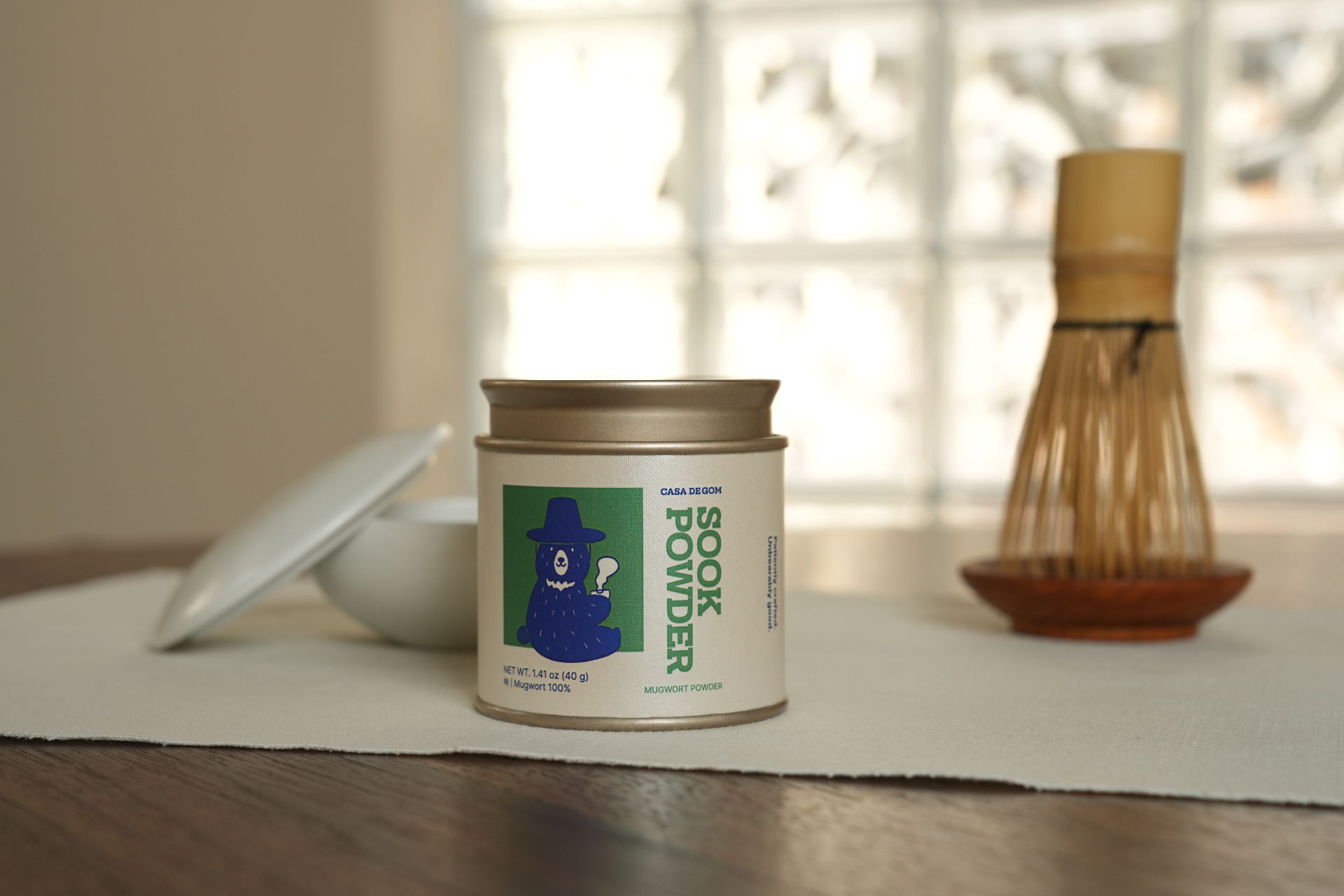 Sook Powder tin on a linen runner beside a bamboo whisk